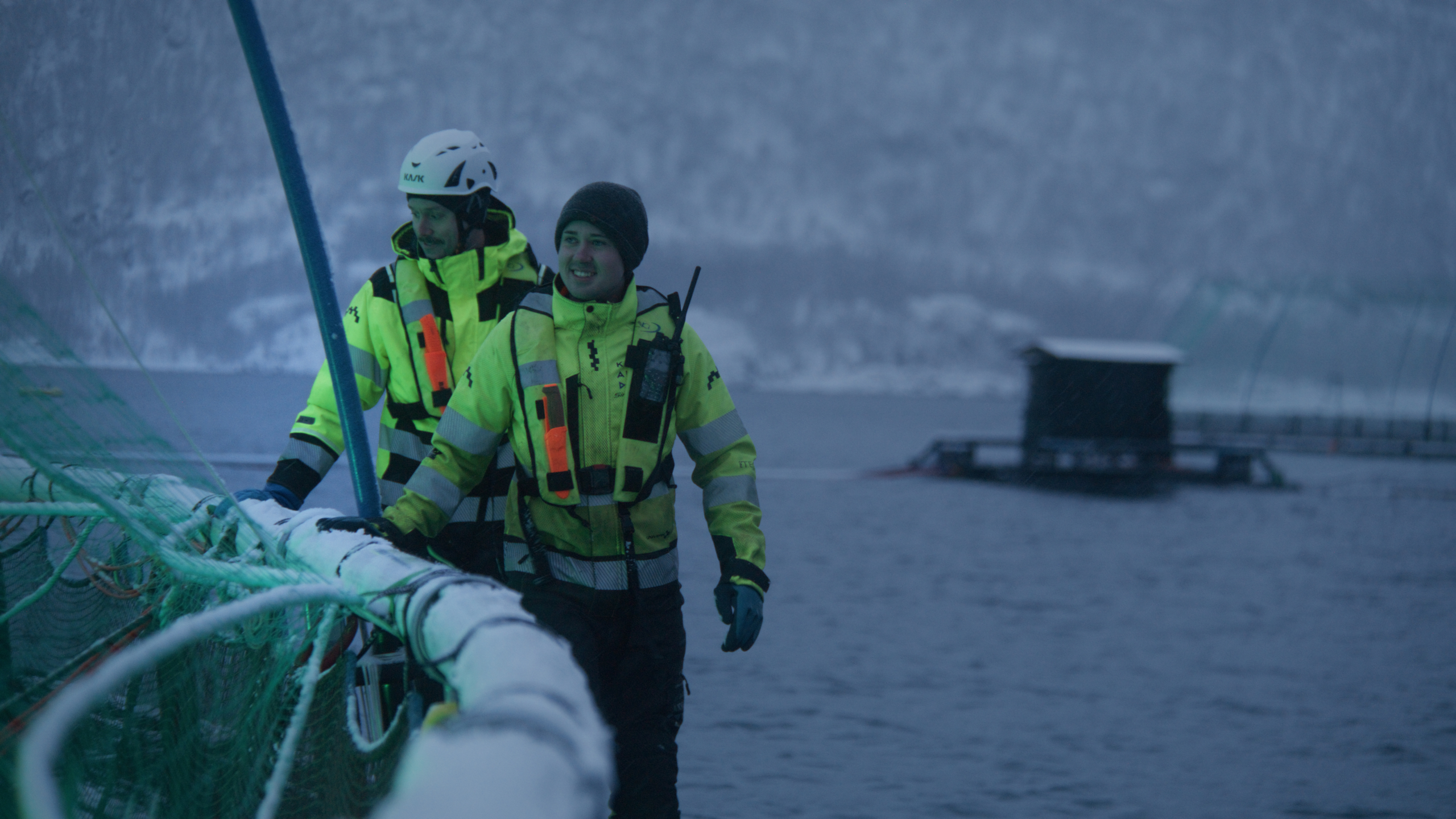 To ansatte i arbeid på merdene ved lokalitet Hallarnes